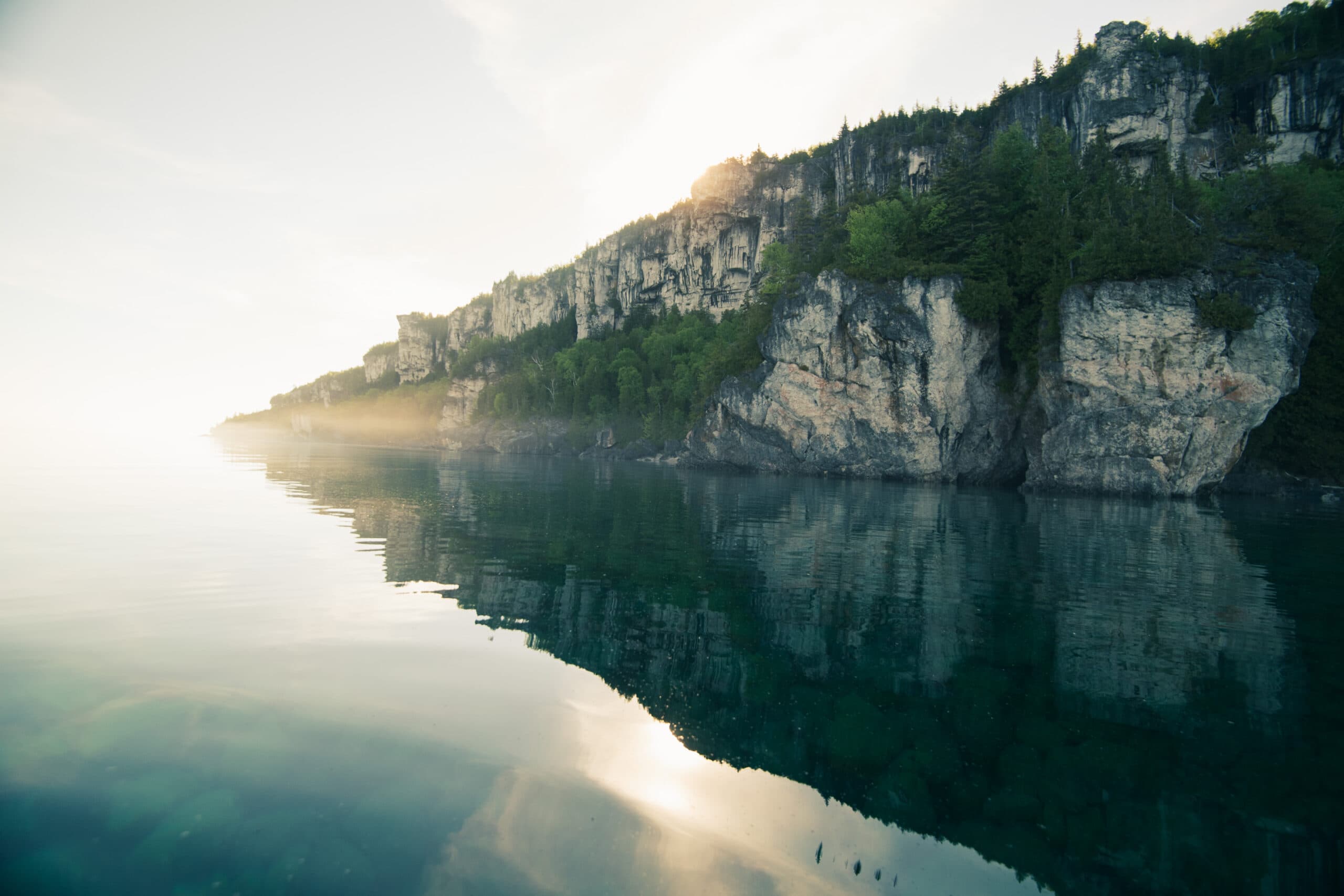 A big rock reflects against the still lake water at sunset